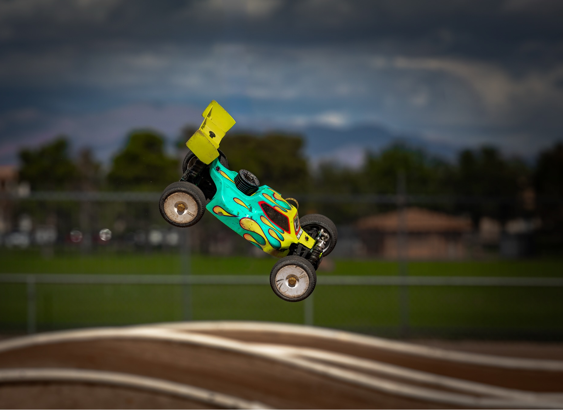 green RC jumping a dirt ramp with the white lines of the track in the background